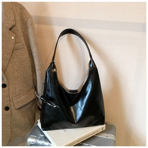 Detail of black glossy leather tote bag with white stitching on a silver suitcase
