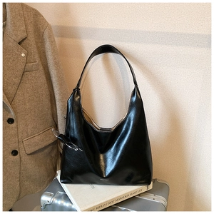 Detail of black glossy leather hobo bag with contrast white stitching and silver logo