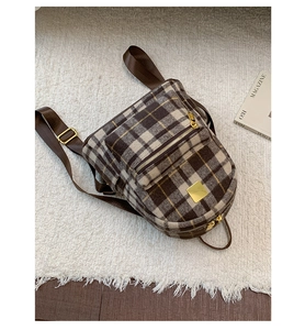 Detail of plaid wool backpack featuring golden zippers and adjustable brown straps