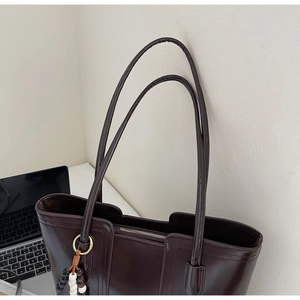 Dettaglio della borsa tote in pelle marrone scuro lucida con ciondolo a perline colorate