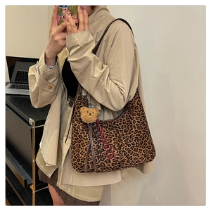 Detail of leopard print hobo bag with brown strap and plush bear charm on a shoulder