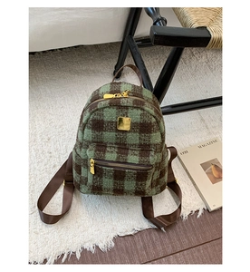 Detail of green and brown plaid plush mini backpack with gold hardware on soft rug