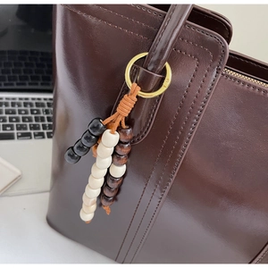 Dettaglio del ciondolo in perline di legno vintage su una borsa tote in pelle marrone