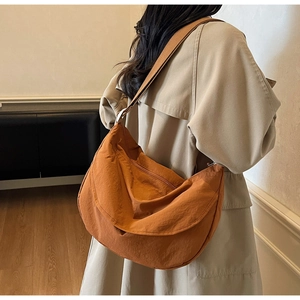 Detail of caramel orange crescent bag showing nylon texture and wide fabric shoulder strap