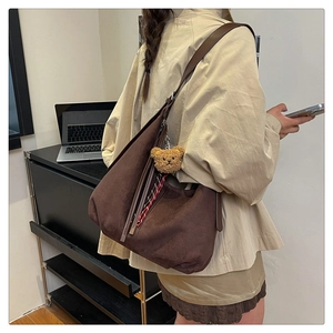 Detail view of a large brown suede tote bag featuring a cute teddy bear charm and ribbon