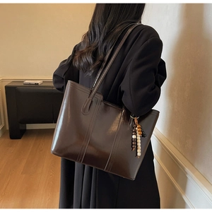 Dettaglio della borsa tote marrone lucida con nappa di perline in legno e doppie tracolle