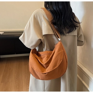 Detail of pumpkin orange nylon dumpling bag showing wide shoulder strap and fabric texture