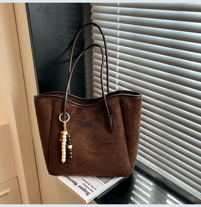 Detail of dark brown suede tote bag featuring fine leather straps and beaded tassel charm