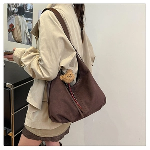 Detail of dark brown suede crescent bag with adjustable strap and plush bear charm