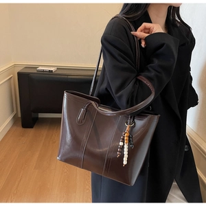Dettaglio di una borsa tote in pelle marrone scuro con ciondolo di perline sul manico