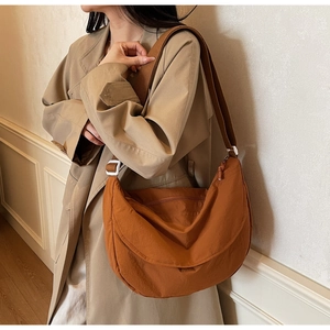 Detail shot of a caramel brown nylon crescent messenger bag on a beige trench coat