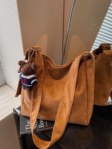 Sac seau hobo en daim marron avec pendentif ourson sur une surface de bois sombre
