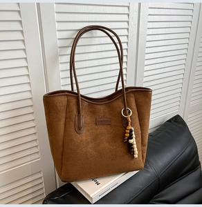 Detail of brown suede tote bag featuring a leather brand tag and vintage tassel ornament