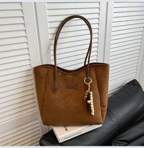 Brown suede tote bag detail featuring dark leather straps and ethnic beaded charm ornament