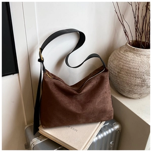 Détail macro d'un sac cabas en daim marron avec bandoulière en cuir noir et décor moderne