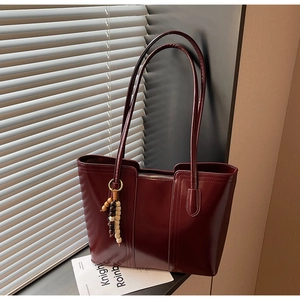 Dettaglio della borsa tote bordeaux lucida con ciondolo di perline e luce naturale