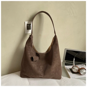 Detailed texture of brown suede tote bag with cylindrical charm in a workplace setting