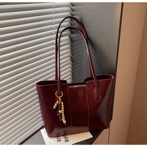 Dettaglio borsa tote bordeaux in finta pelle con perline in legno vicino alle tapparelle