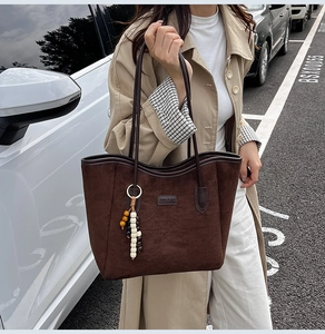 Detail of dark brown suede tote bag featuring a beaded metal ring charm and branding