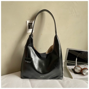 Close-up of black polished leather tote bag with brand logo and small hanging pouch