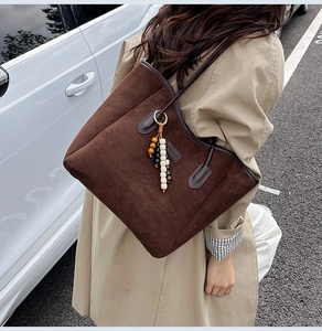Detail of dark brown suede tote bag featuring unique wooden bead charms and shoulder strap