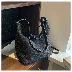 Close-up of leopard print canvas tote bag with black leather shoulder strap on wooden table