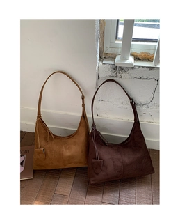 Detail view of large suede tote bags in tan and dark brown against a vintage white wall