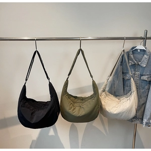 Three quilted nylon crescent bags in black, olive green, and cream white displayed hanging