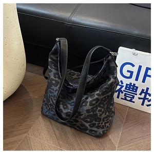Detail of leopard print canvas tote bag with black leather handles on wooden floor