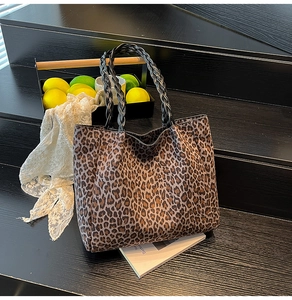 Detail of leopard print tote bag featuring woven leather handles on a dark wood background