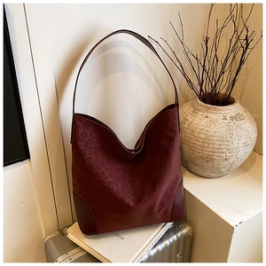 Close-up of a burgundy leopard embossed tote bag placed on books in a cozy setting