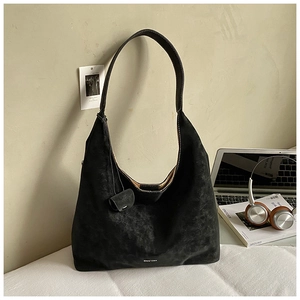 Detail of black suede Hobo tote bag with mini purse charm on minimalist white desk