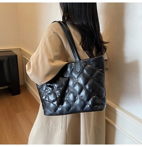 Detailed view of black quilted tote bag with floral embroidery on a glossy leather finish