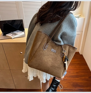 Close-up of a brown matte tote bag featuring a beaded tassel and miao & she metal label