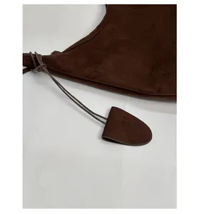 Detailed macro view of deep brown suede handbag showing decorative pendant and seam stitching