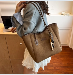 Brown suede tote bag detail with wooden bead tassel and delicate leather brand patch