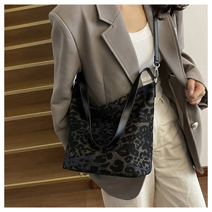 Detailed close-up of leopard print canvas fabric and black leather strap on a hobo bag