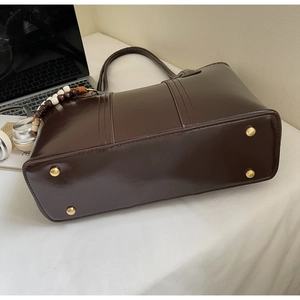 Dettaglio della base di una grande borsa tote marrone scuro con piedini in metallo oro