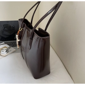 Dettaglio borsa shopper marrone scuro lucida con pendente di perline in legno