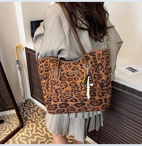 Close-up of leopard print tote bag featuring wooden bead charm and brand logo detail
