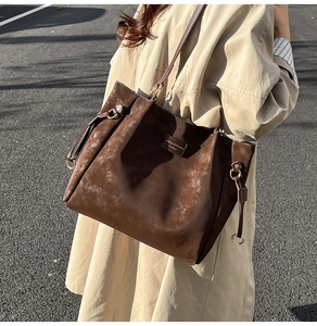 Detail of a large brown matte leather tote bag with side drawstrings and logo patch