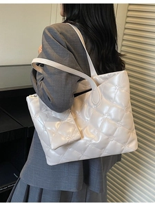 Quilted cream shoulder bag with floral embroidery and matching charm on a sleek counter