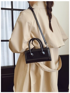 Model wearing a black glossy leather mini bag with beige trench coat, side view detail