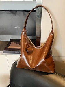 Retro large brown hobo bag in soft oiled leather leaning on a leather chair