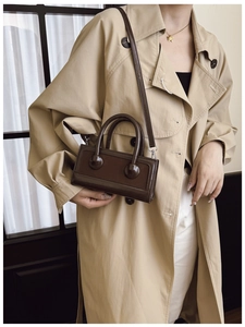 Detailed view of a vintage dark brown leather crossbody bag styled with a trench coat