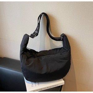 Detail of black quilted nylon crescent bag with embroidered logo strap on books