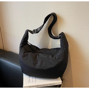 Detail of black quilted puffer bag showing wide adjustable strap with white embroidery