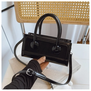 Close-up of a black tote bag with mixed glossy and matte leather held by the handle