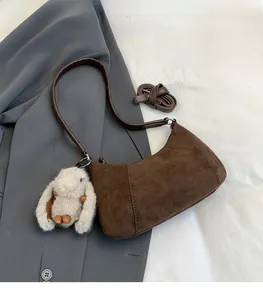 Close-up of brown suede hobo bag with adjustable leather strap and plush rabbit charm