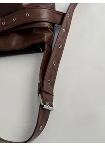 Detail of adjustable wide shoulder strap with silver eyelets on brown leather tote bag